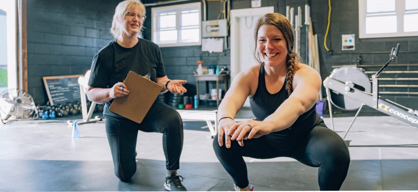 CrossFit Rush coach assisting athlete during strength training workout in the gym
